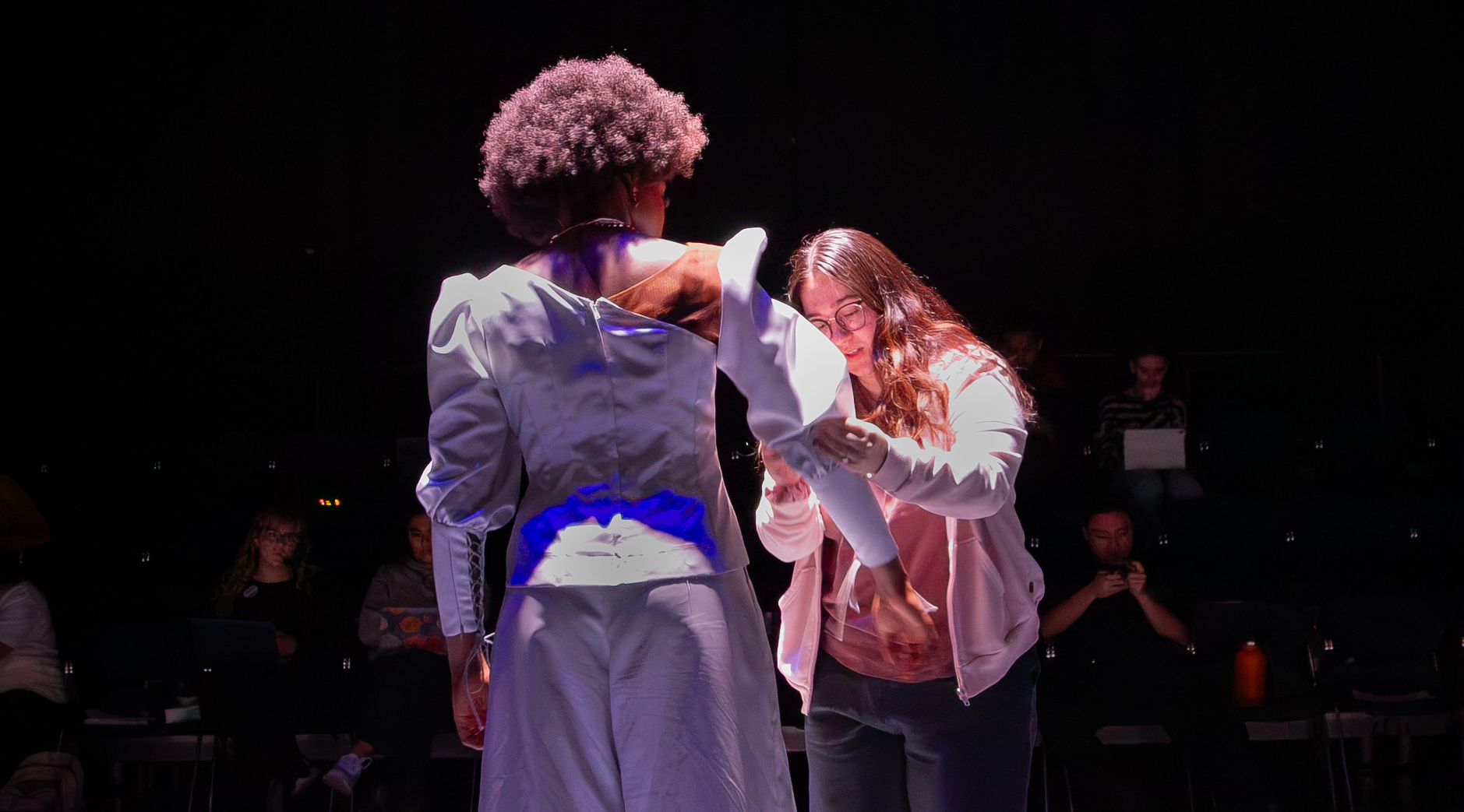 The costume designer adjusts an actor's costume on stage during rehearsal
